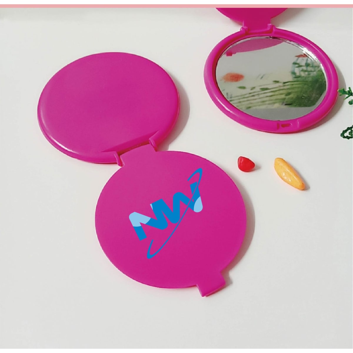 A round, pink folding mirror with a reflective surface and a logo on the outer casing.