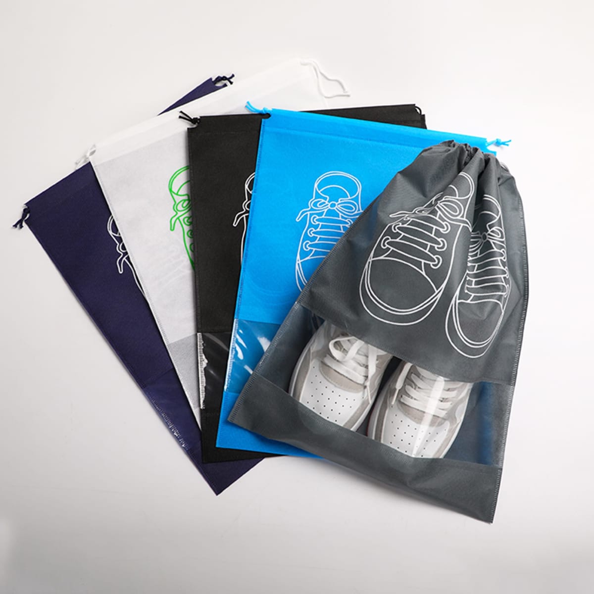 A collection of non-woven drawstring bags in various colours, featuring clear windows and shoe graphics.