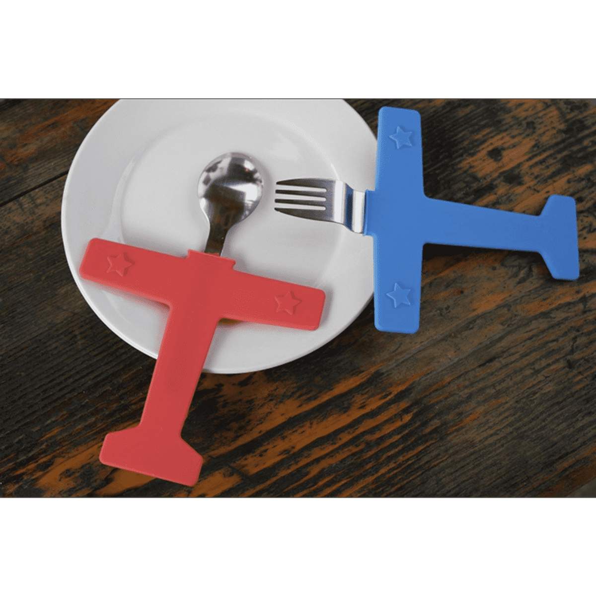 A red airplane-shaped spoon and a blue airplane-shaped fork on a white plate against a wooden background.