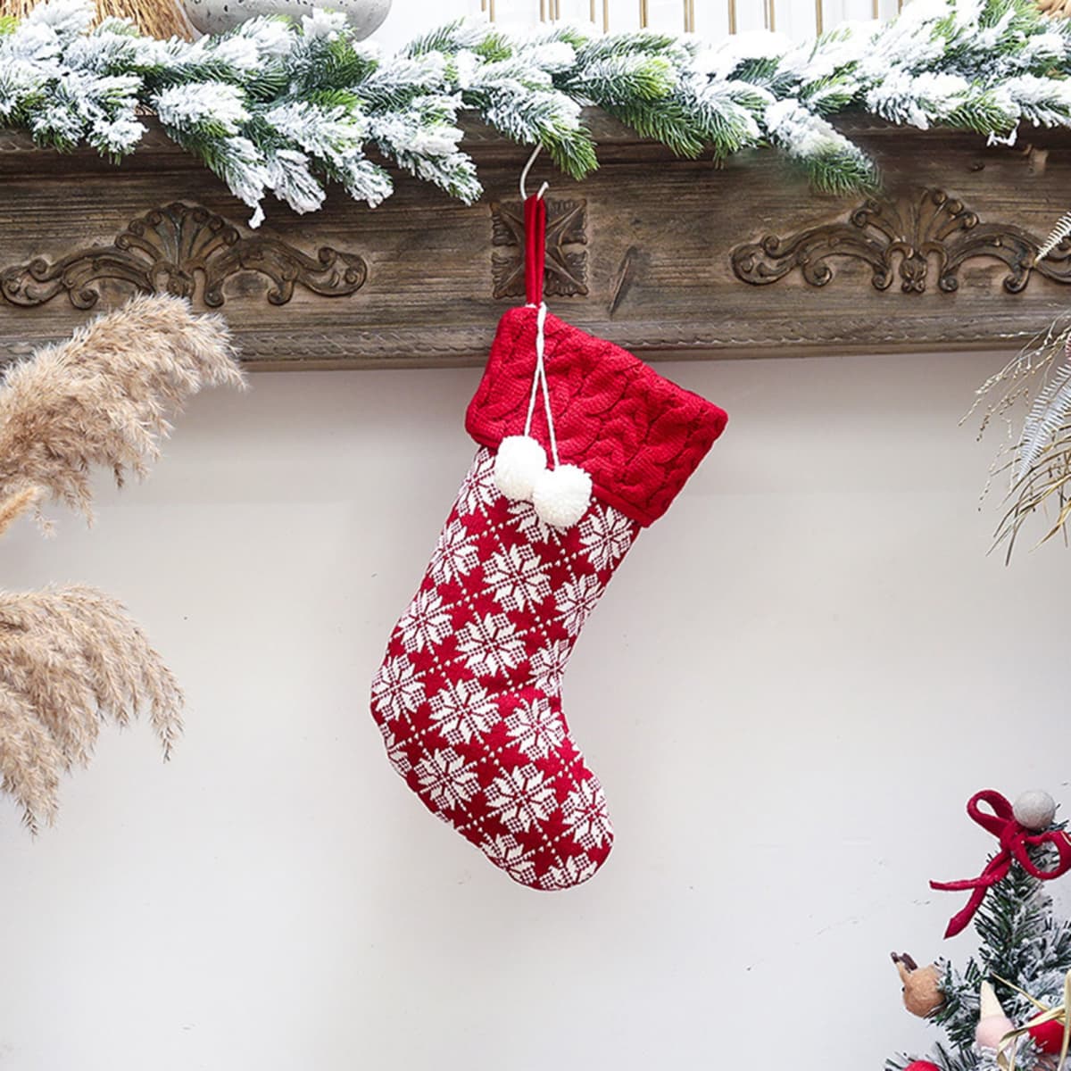 A Christmas stocking in red and white featuring a snowflake pattern, adorned with fluffy white pom-poms.