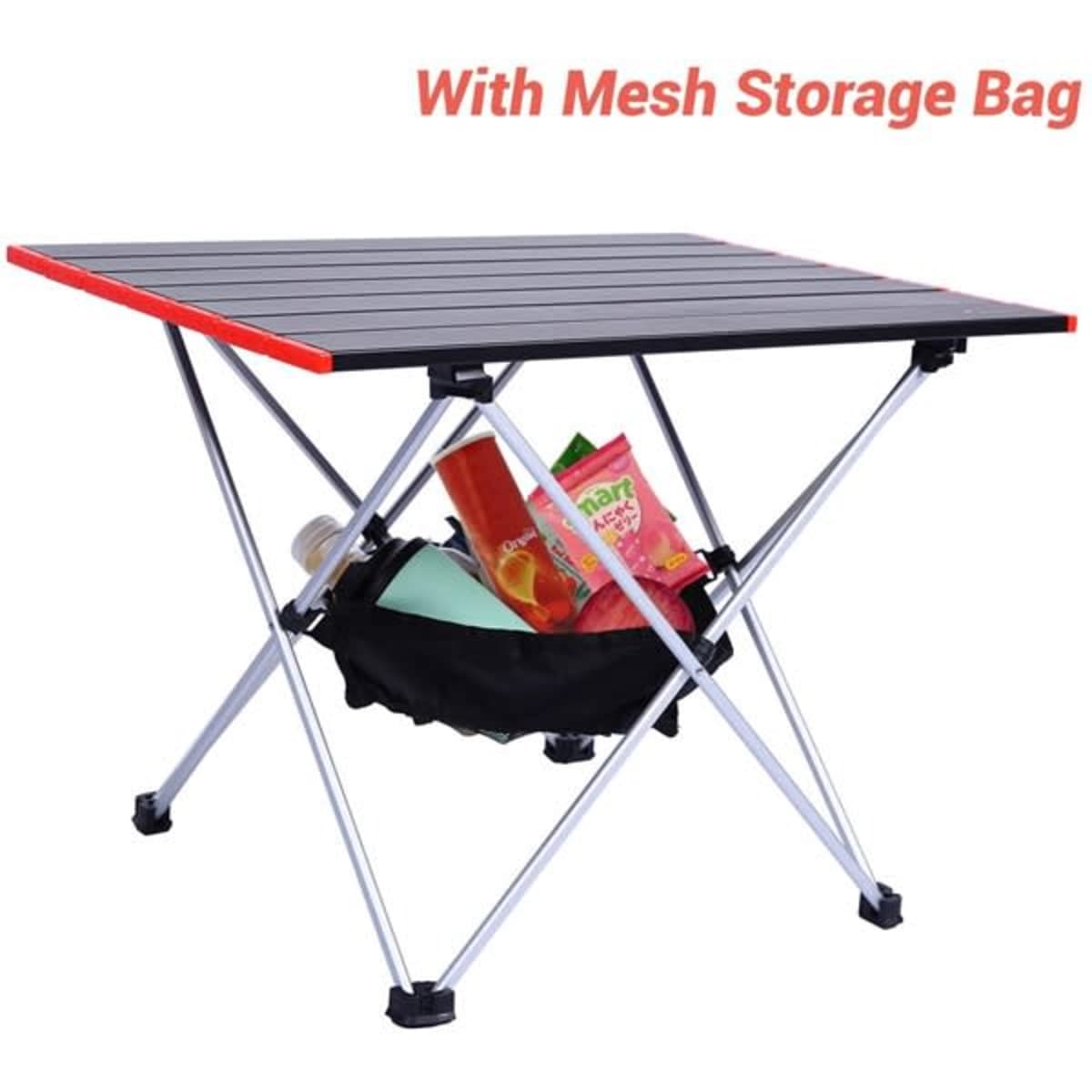 A portable camping table with a black top, red edges, and a mesh storage bag underneath filled with items.