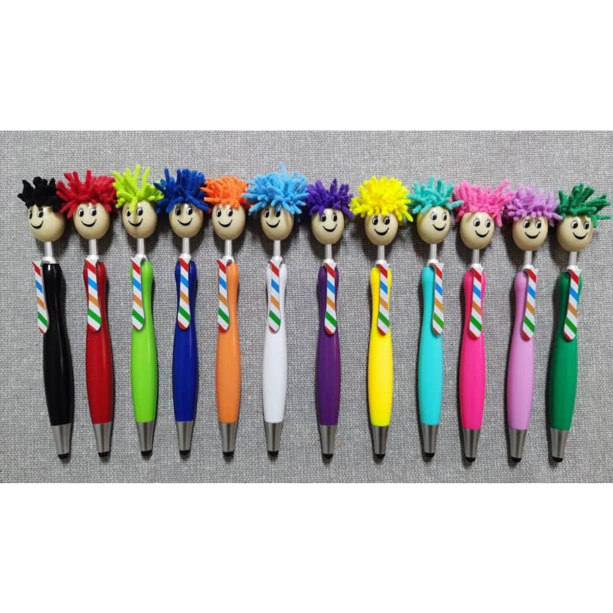 A collection of colourful stylus pens with playful, fuzzy-haired tops, featuring various bright colours and cheerful faces.