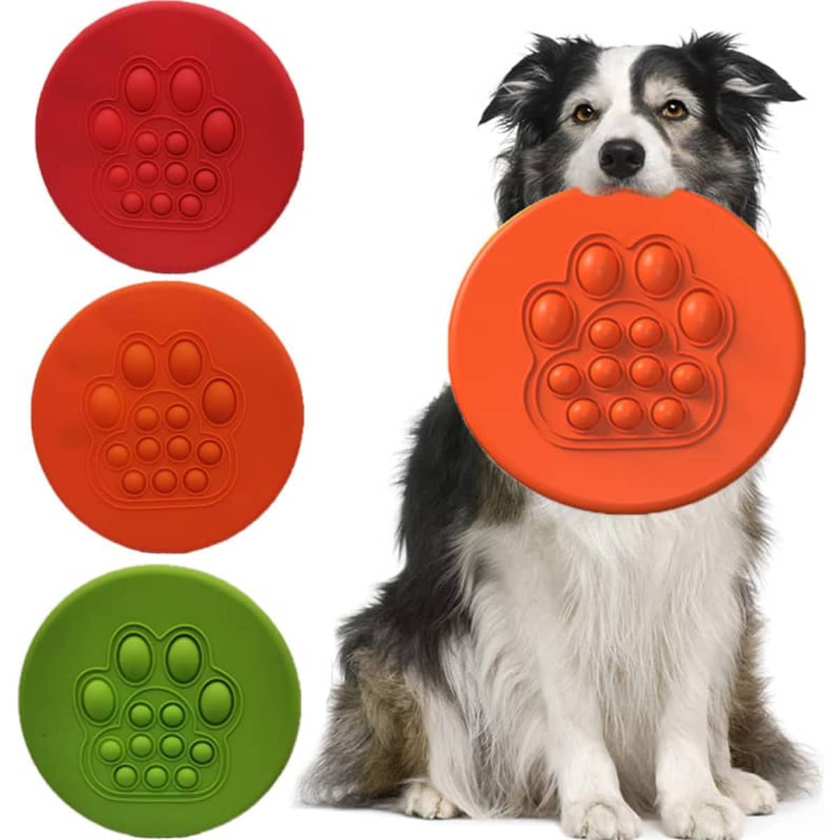 A dog holds a large orange flying disc, surrounded by red, orange, and green discs featuring a paw print design.