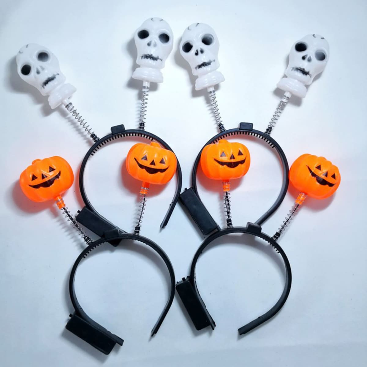 A black headband featuring orange pumpkins and white skulls on springs. Ideal for Halloween celebrations.