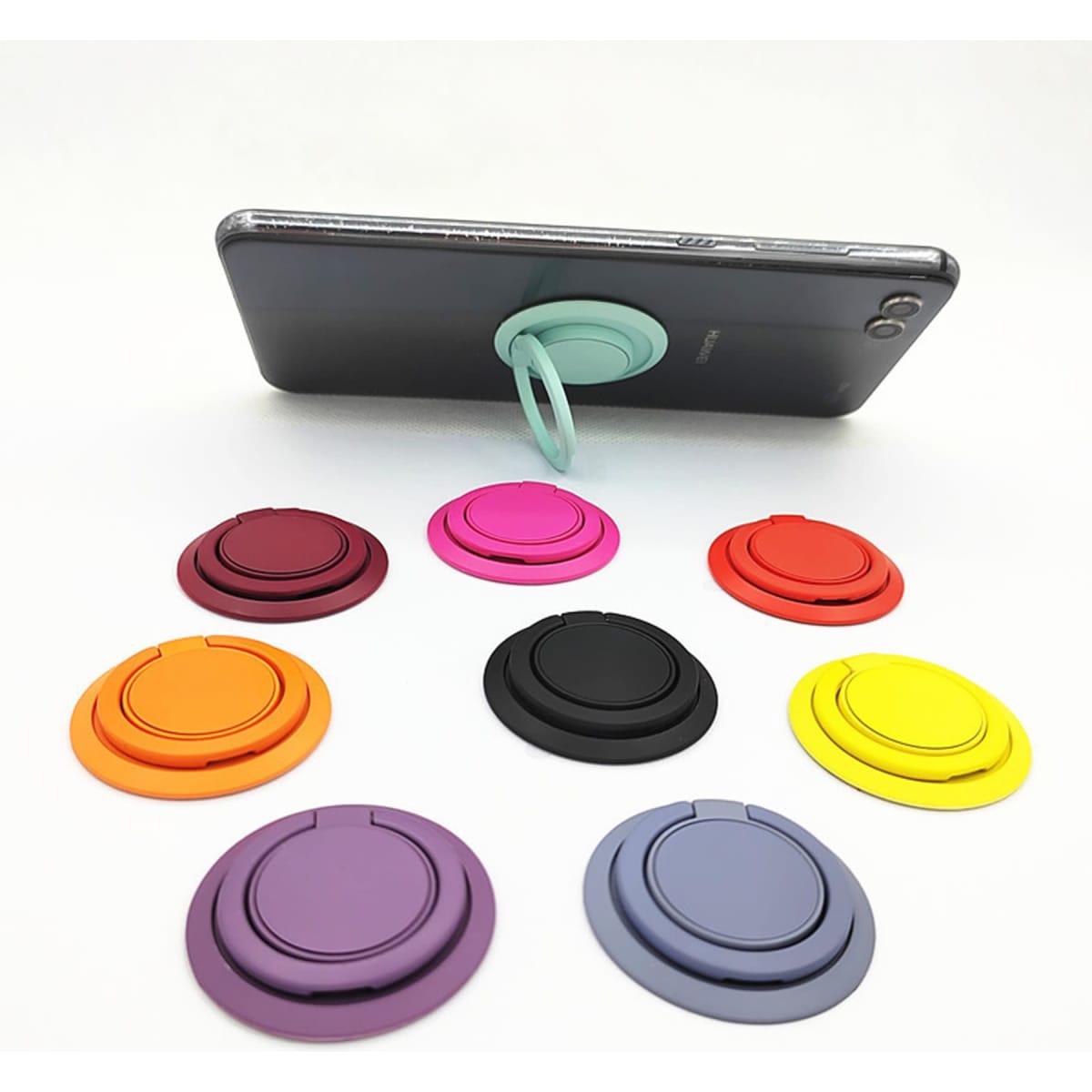 A smartphone with a turquoise ring holder, surrounded by eight colourful cell phone holders in various shades.