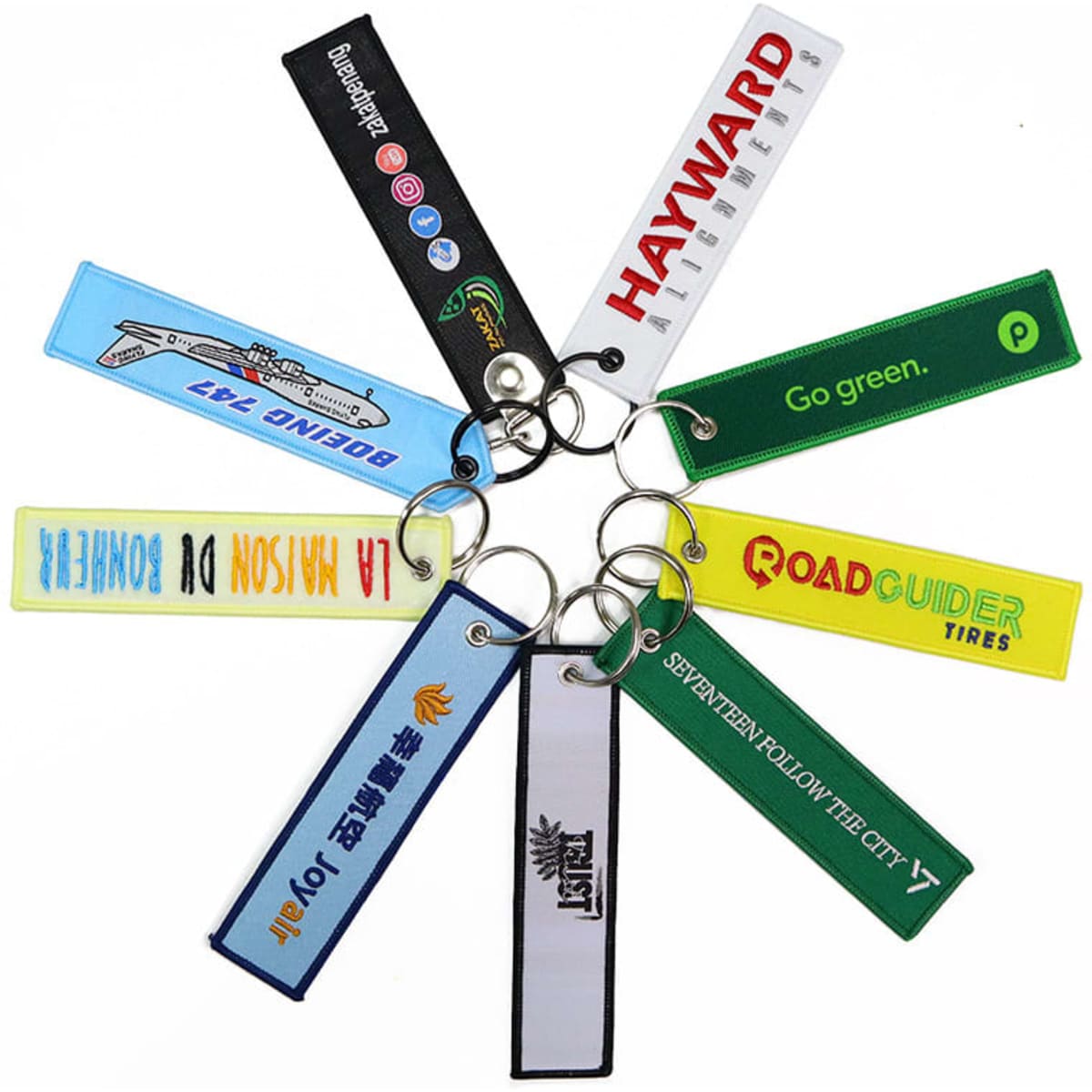 A collection of fabric woven keychains in various colours, each featuring custom logo embroidery and metal rings.