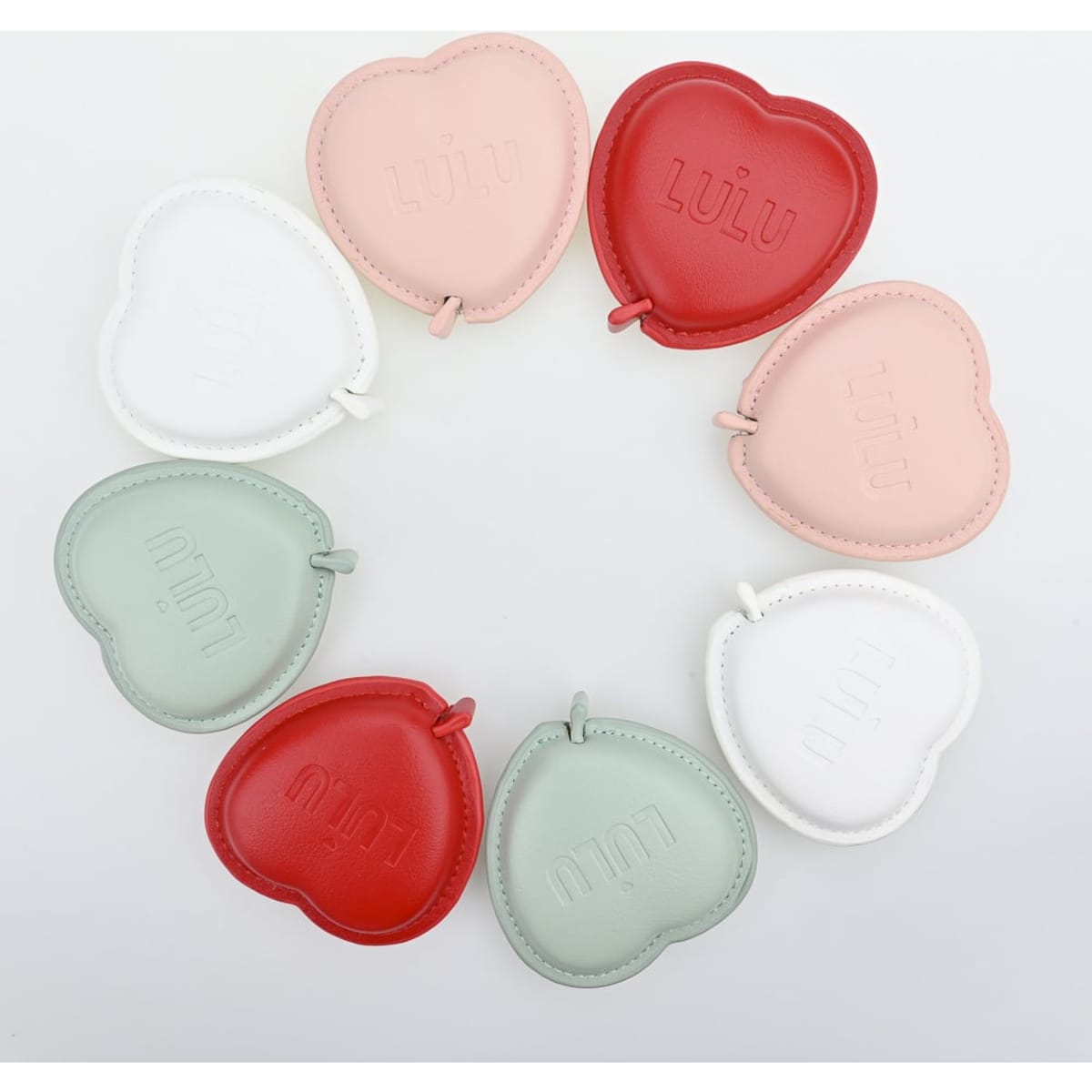 A collection of heart-shaped measuring tapes in red, pink, white, and green, arranged in a circular pattern.