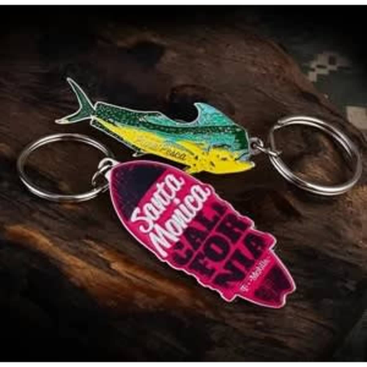A colourful soft enamel keychain featuring a fish design and a pink surfboard, both attached to silver keyrings.