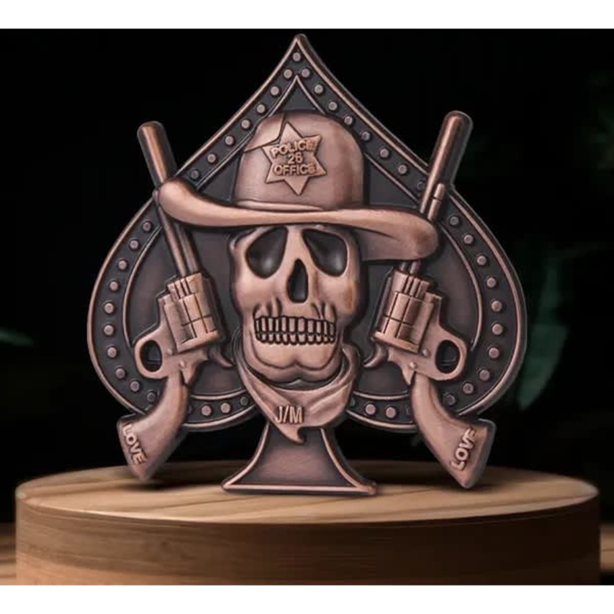 A decorative 3D die cast lapel pin in bronze, featuring a skull with guns and a police hat, shaped like a spade.