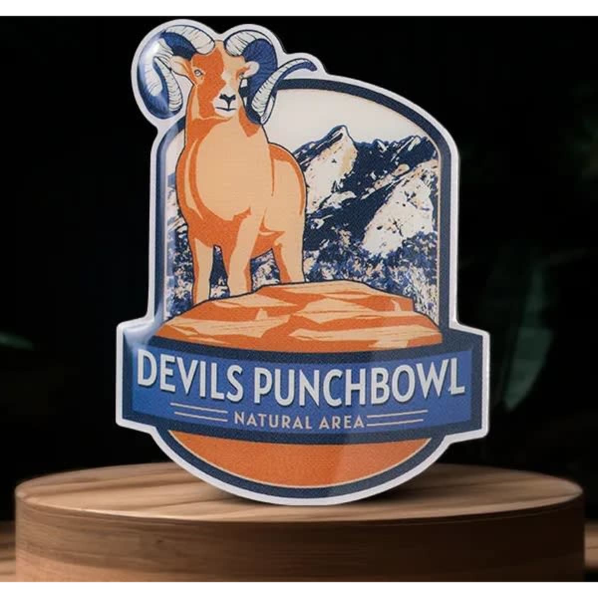 An orange ram stands on a rock, with mountains in the background. Features a blue logo with "Devils Punchbowl."
