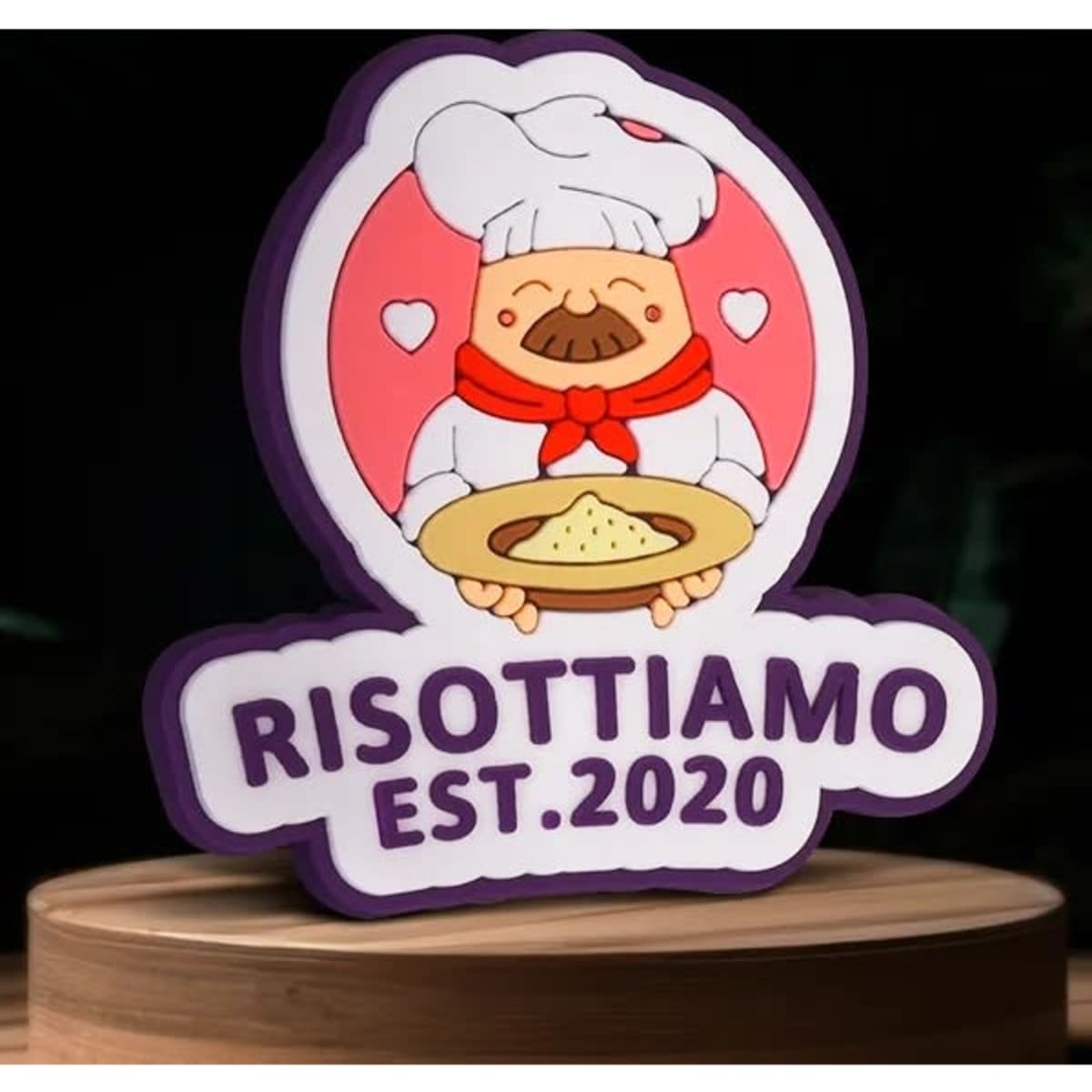 A colourful PVC lapel pin featuring a cartoon chef holding a plate of risotto, with the text "RISOTTIAMO EST. 2020" and a logo.