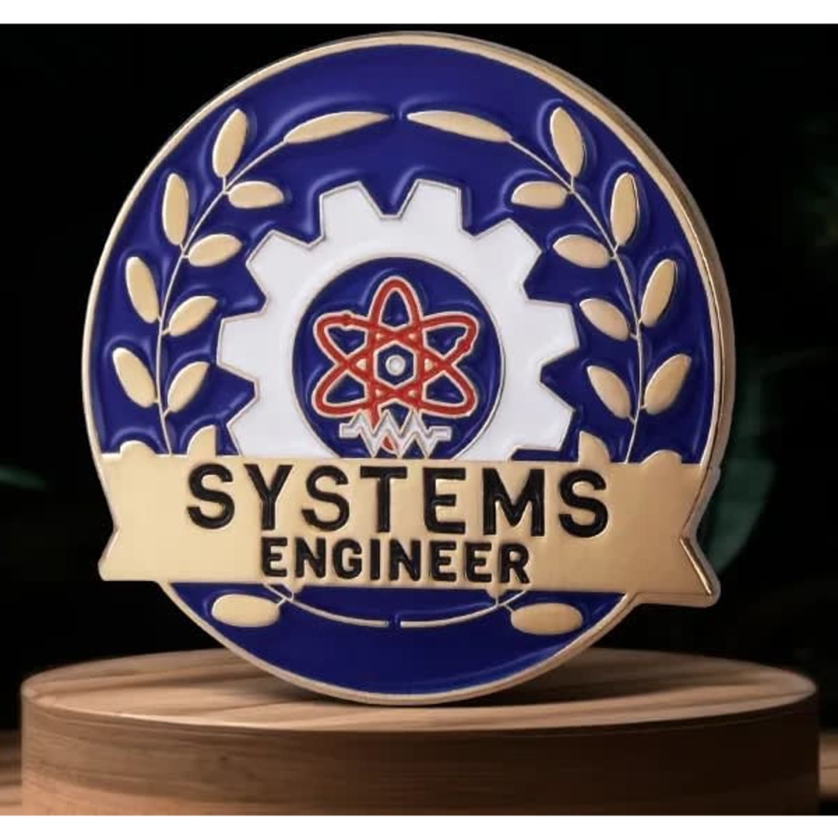 A brass lapel pin featuring a blue and white design with a gear and atom symbol, labelled "SYSTEMS ENGINEER."
