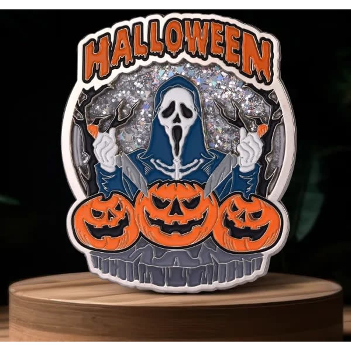 A Halloween-themed lapel pin featuring a ghostly figure holding two knives, surrounded by carved pumpkins in orange and black.