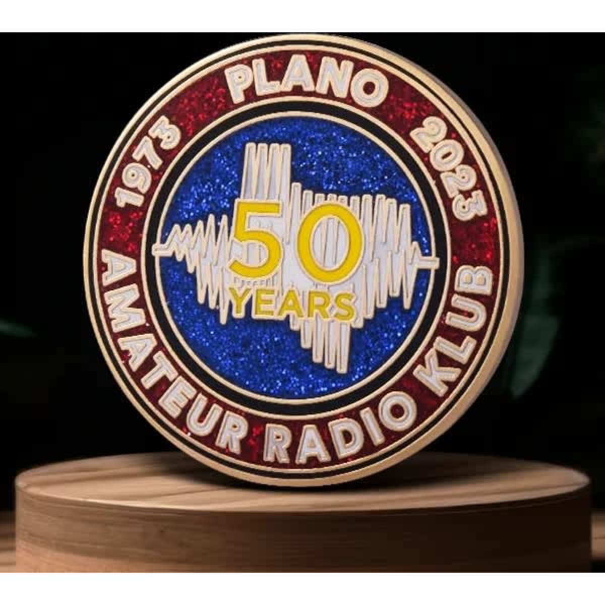 A circular lapel pin featuring red and blue glitter, commemorating 50 years of the Plano Amateur Radio Klub, with a logo.