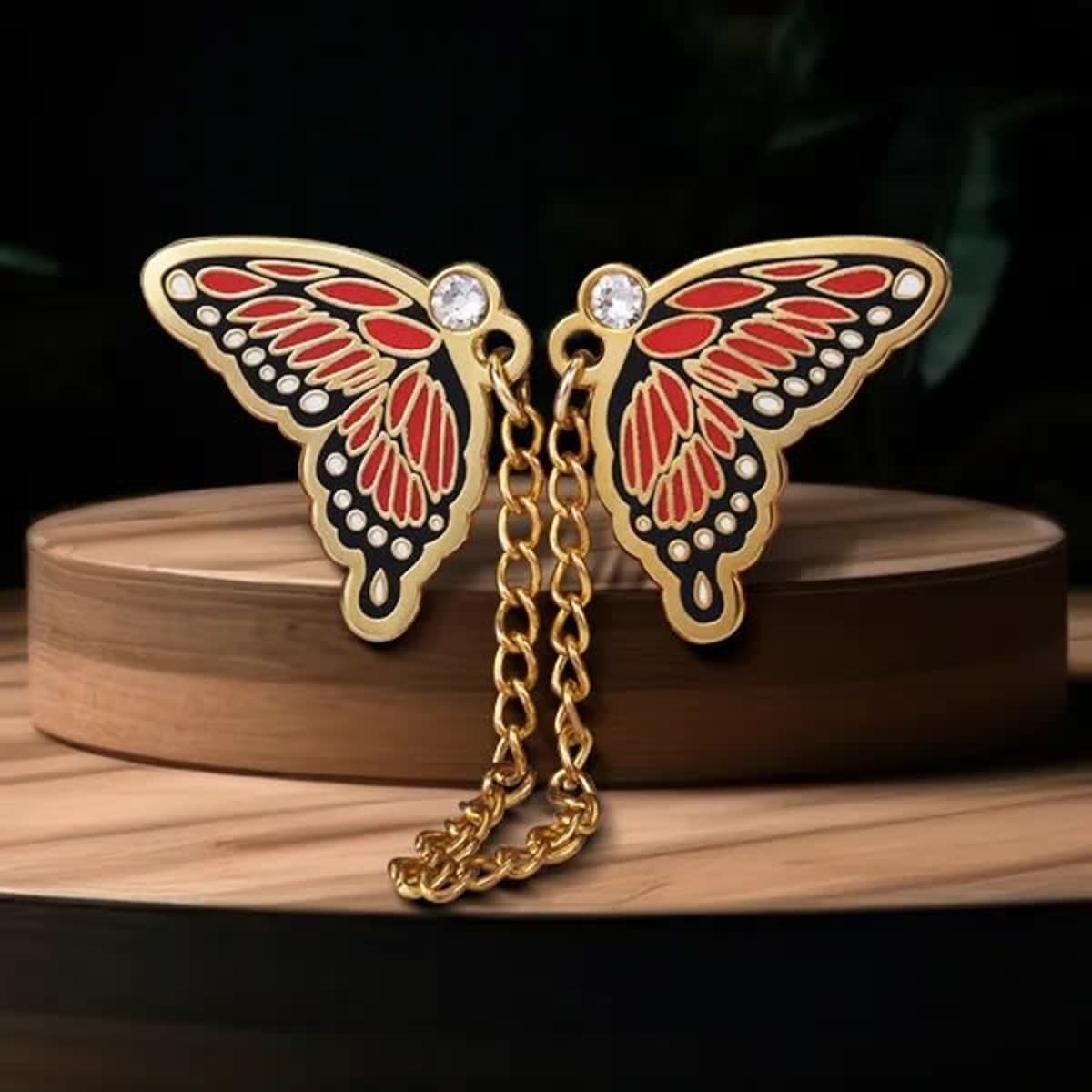 A pair of gold butterfly lapel pins with red and black detailing, connected by a gold chain.