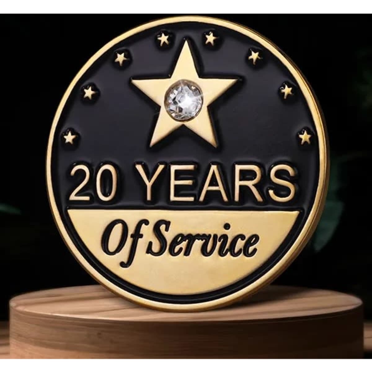 A gold and black lapel pin featuring a star and a rhinestone, commemorating 20 years of service.
