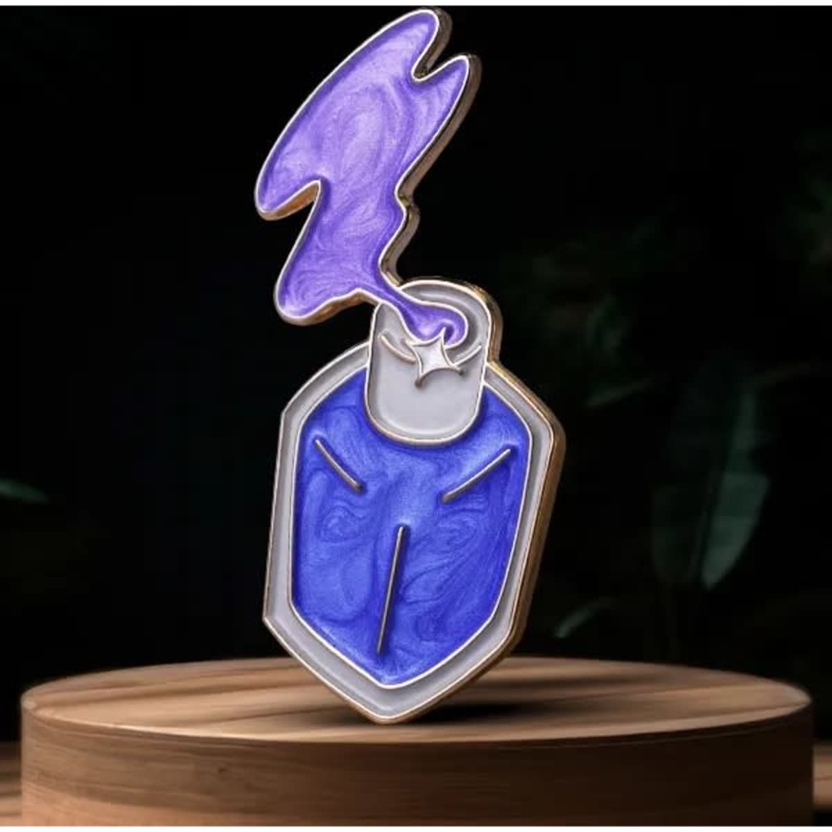 A lapel pin with a pearlescent purple and blue design, featuring a stylised shield shape and a smoke-like top.