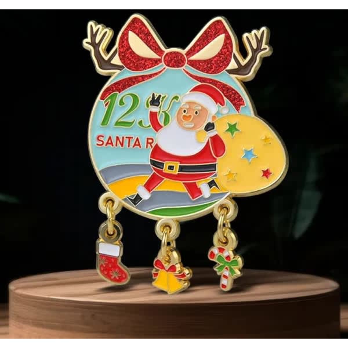 A festive lapel pin featuring Santa Claus, a bow, and dangling charms including a stocking, bell, and candy cane.