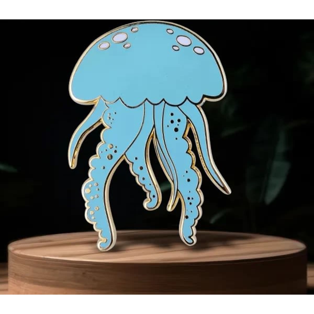 A blue glow-in-the-dark lapel pin shaped like a jellyfish, displayed on a wooden surface.