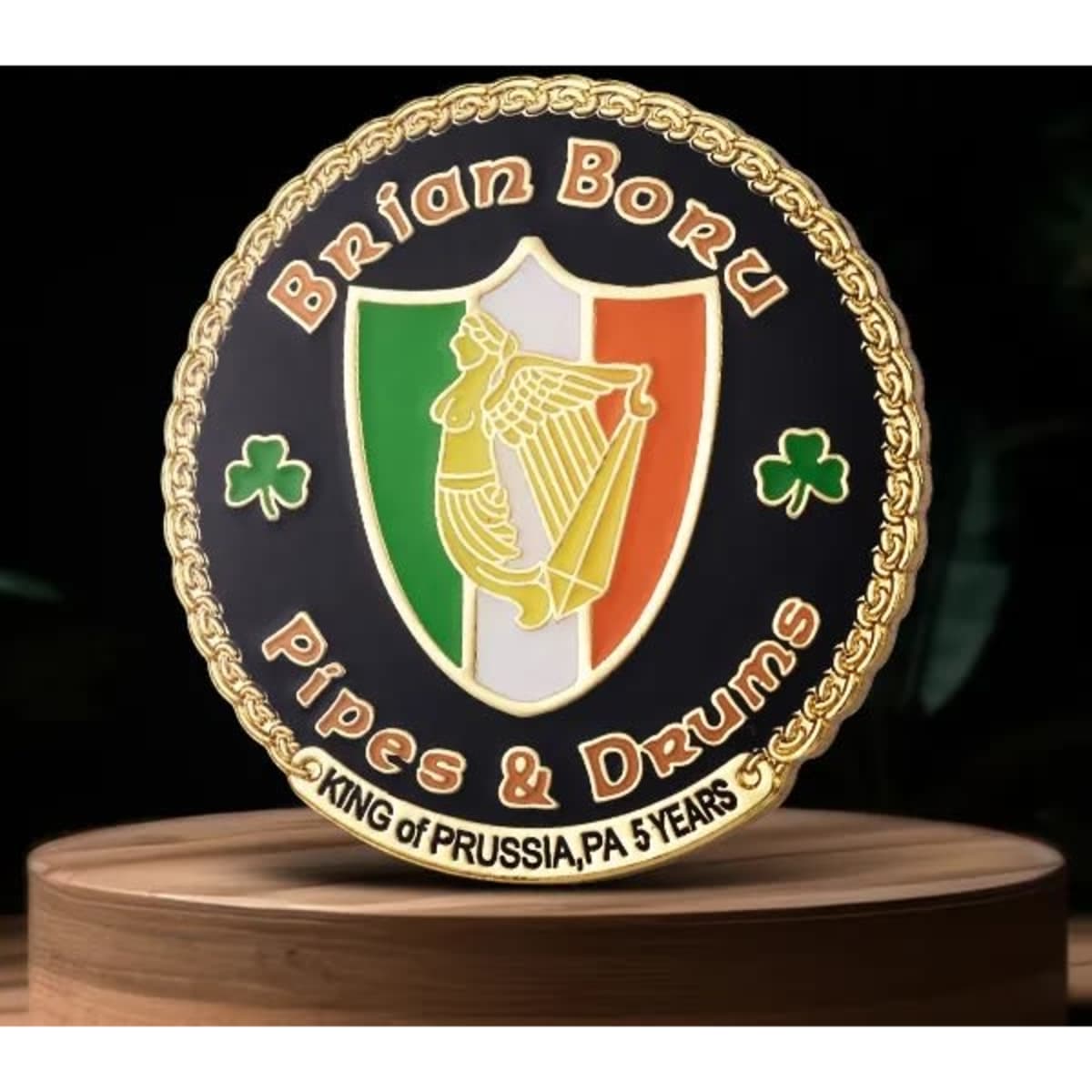 A round lapel pin featuring an emblem with the colours green, white, and orange, and decorated with a logo.