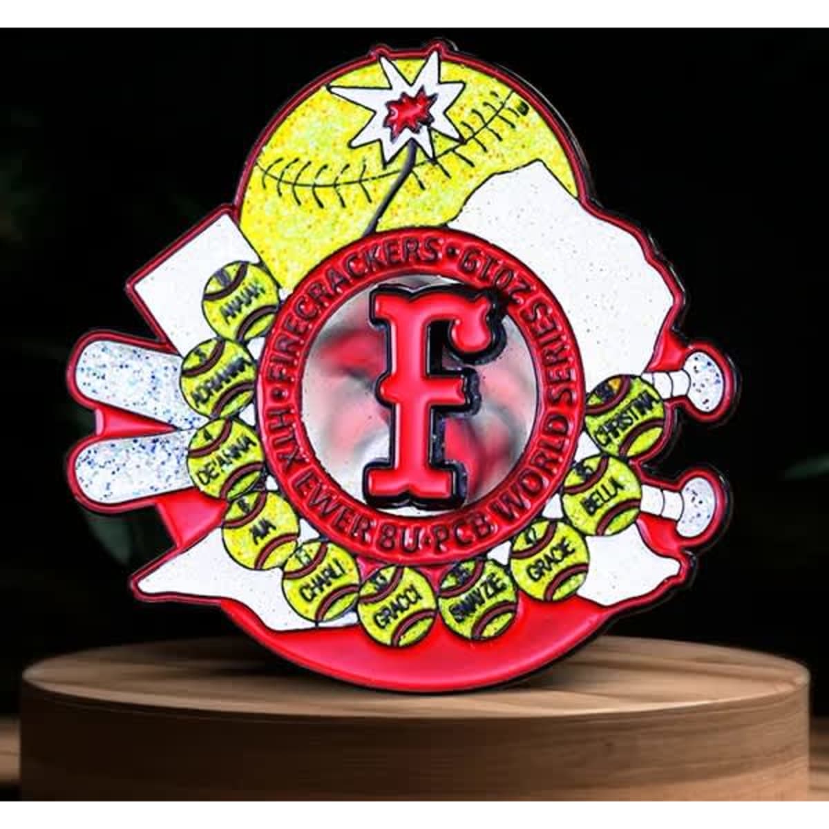 A vibrant spinner lapel pin featuring a red "F" with sports motifs, including baseballs and fireworks against a colourful background.