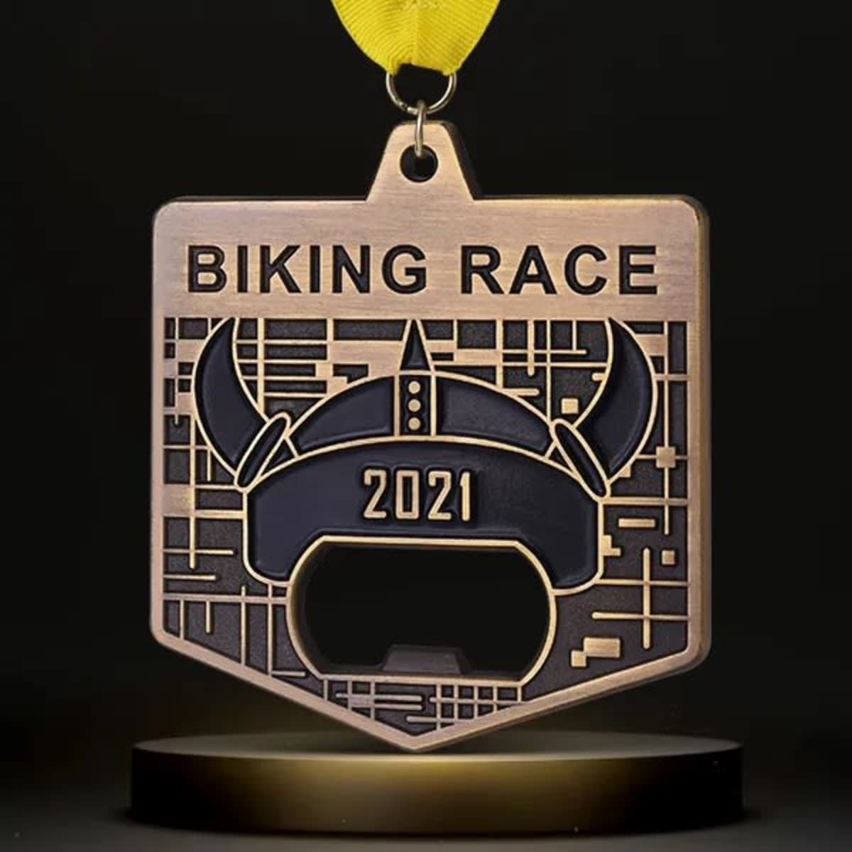 A drink bottle opener medal in bronze with a viking helmet design and a yellow ribbon, marked for a biking race.