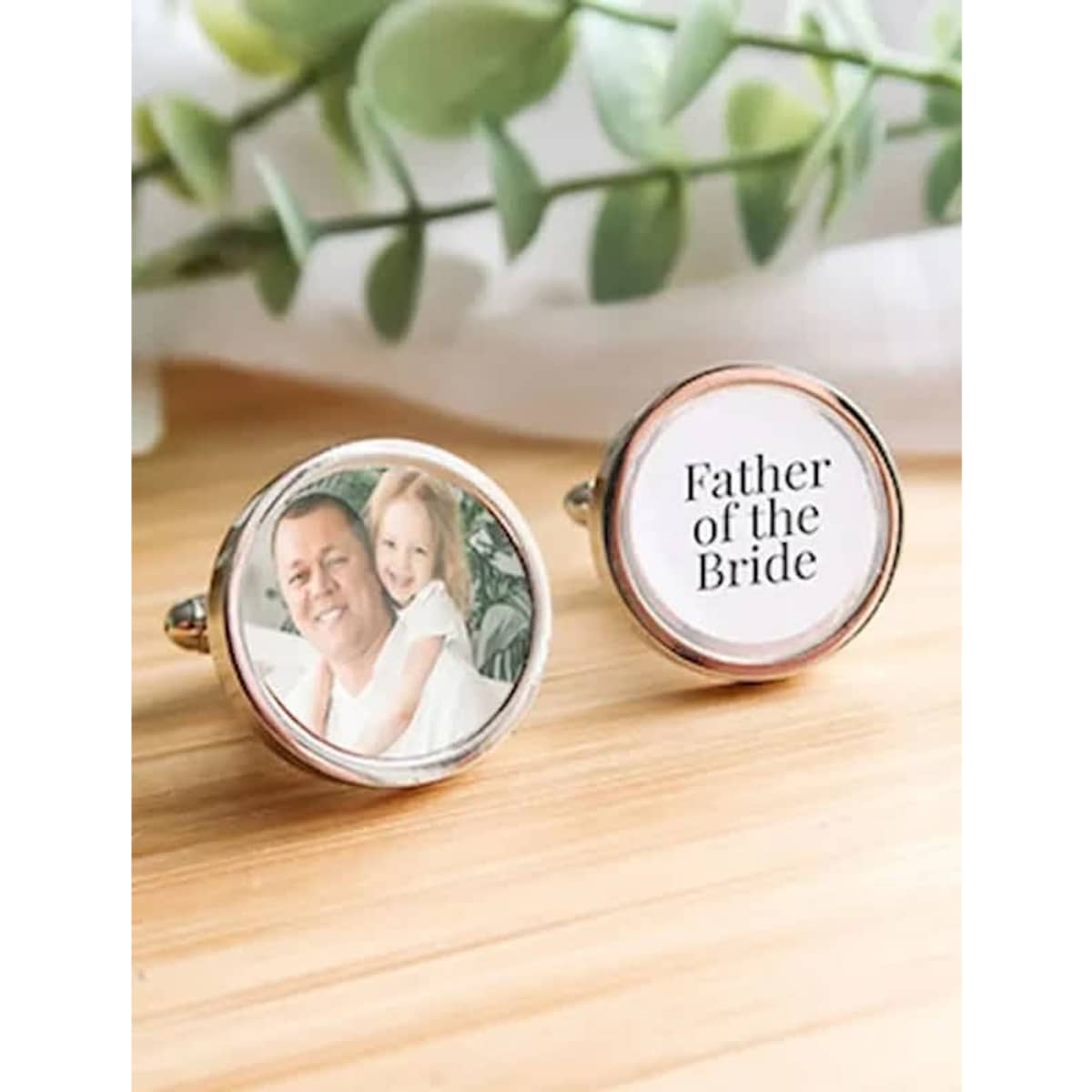Custom cufflinks featuring a photo and text, with a silver finish and a round design, surrounded by greenery.