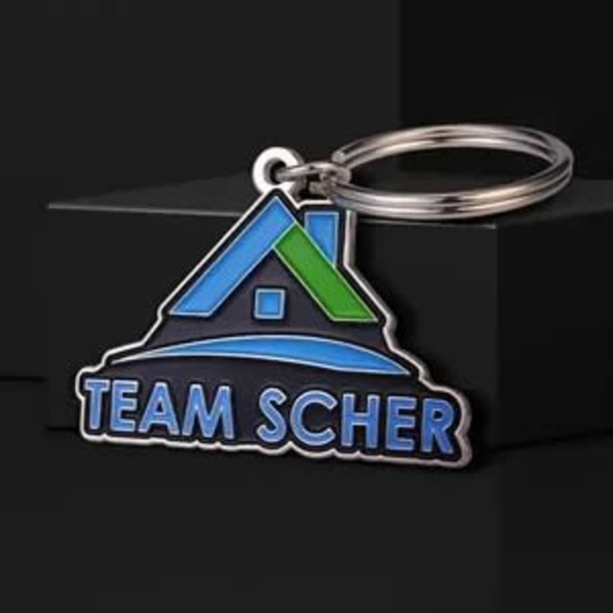 A soft enamel keychain featuring a house design with blue and green colours, attached to a silver keyring.