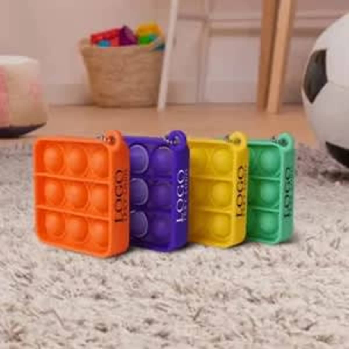 Four mini push pop bubble keychains in orange, purple, yellow, and green arranged on a light carpeted surface.