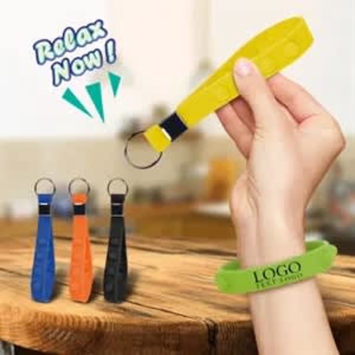 A hand holds a yellow Push Pop stress reliever keychain, with blue, orange, and black variants displayed nearby.