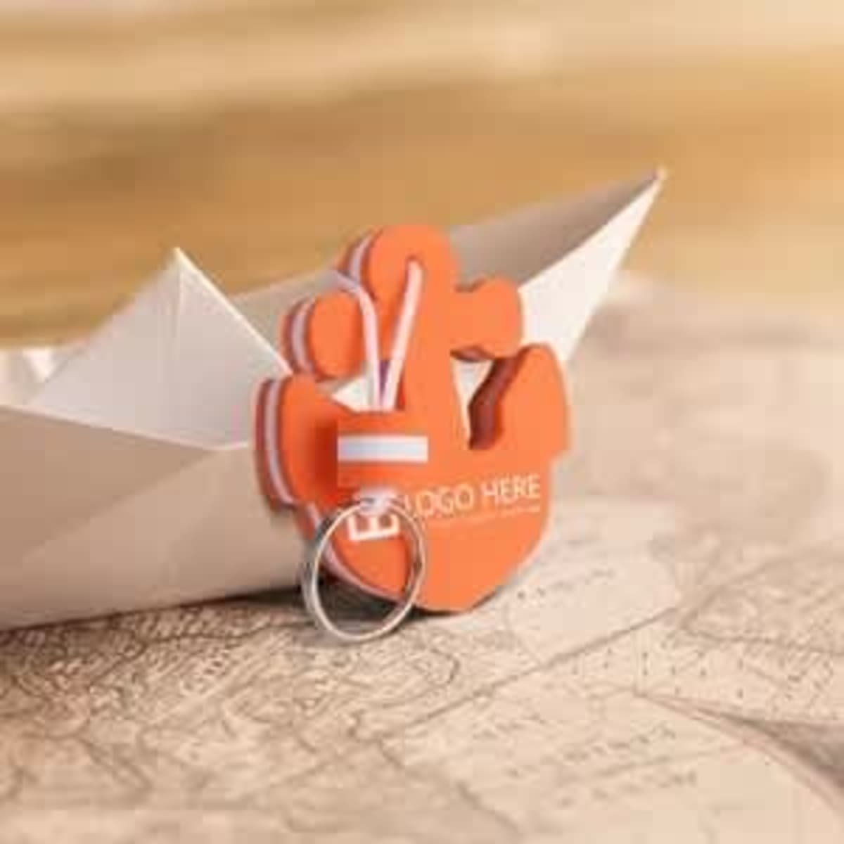 An orange foam anchor keytag with a keyring, resting beside a paper boat on a textured map background.