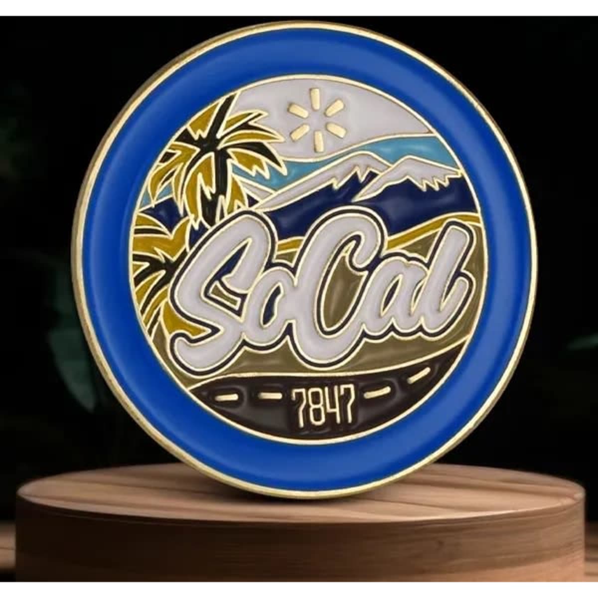 A blue and gold lapel pin featuring palm trees and mountains with "SoCal" and "7847" designs.