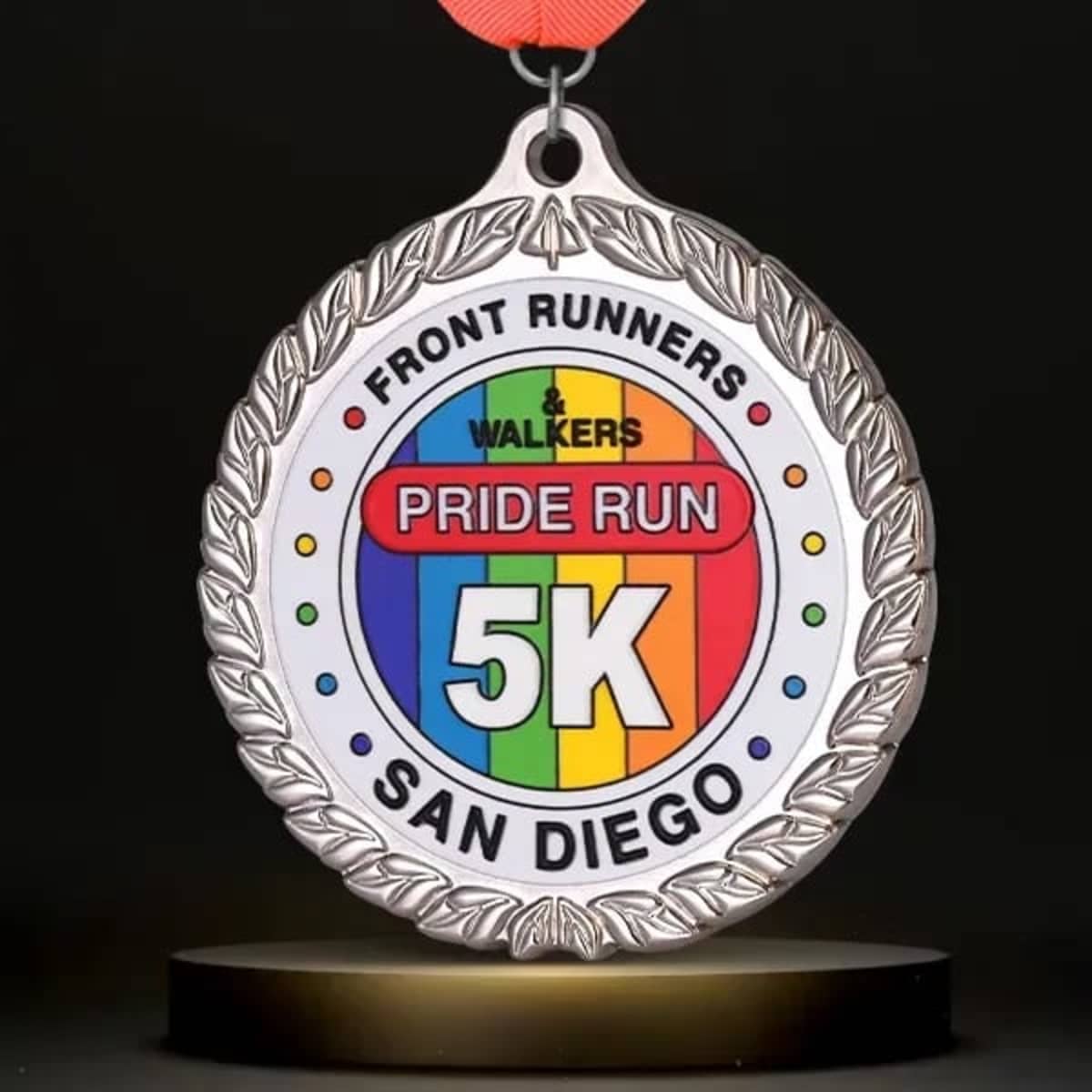 A medal with a silver border, featuring a rainbow design, and a red ribbon for the 5K Pride Run in San Diego.