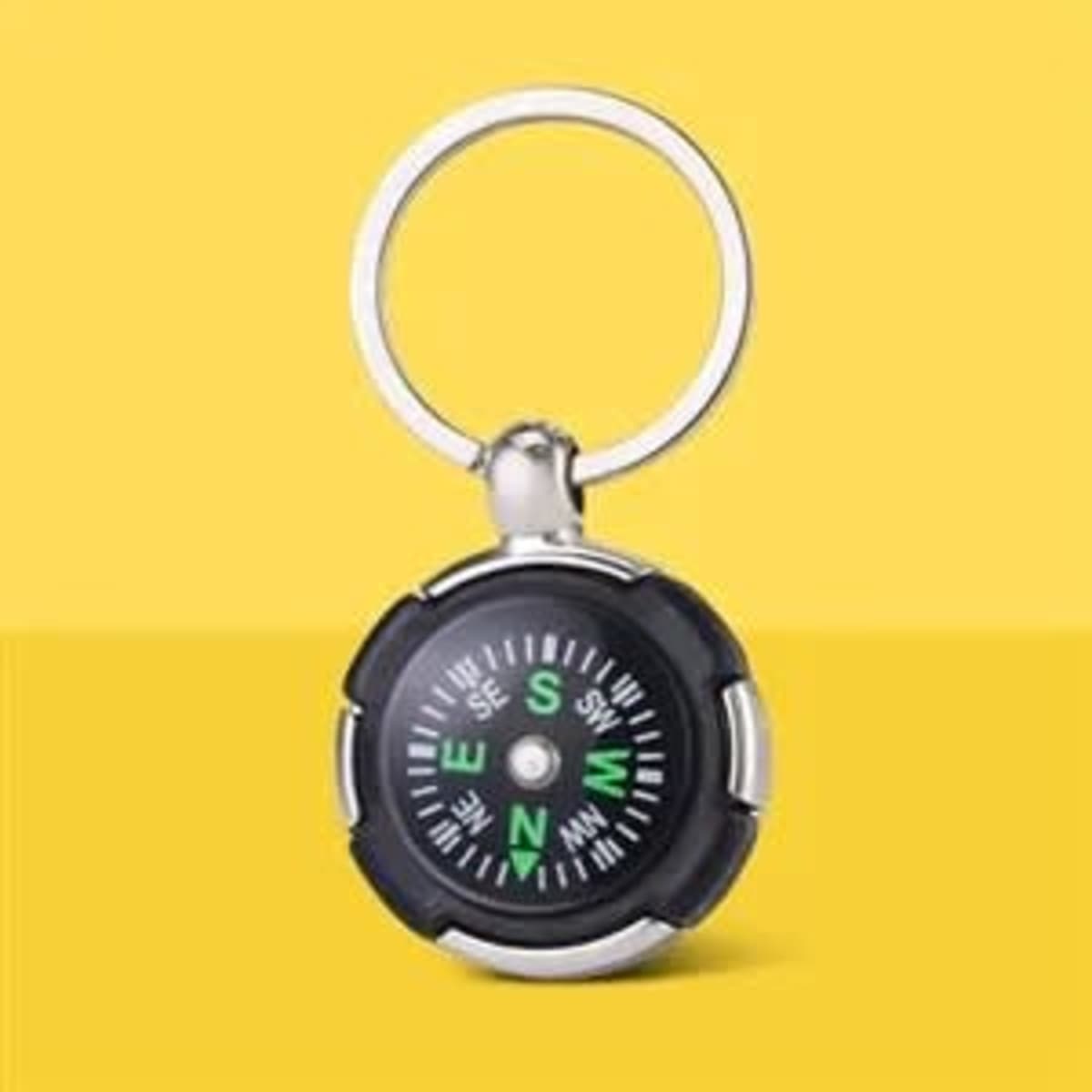 A black mini compass keychain with a silver loop, displaying compass directions in green on a yellow background.