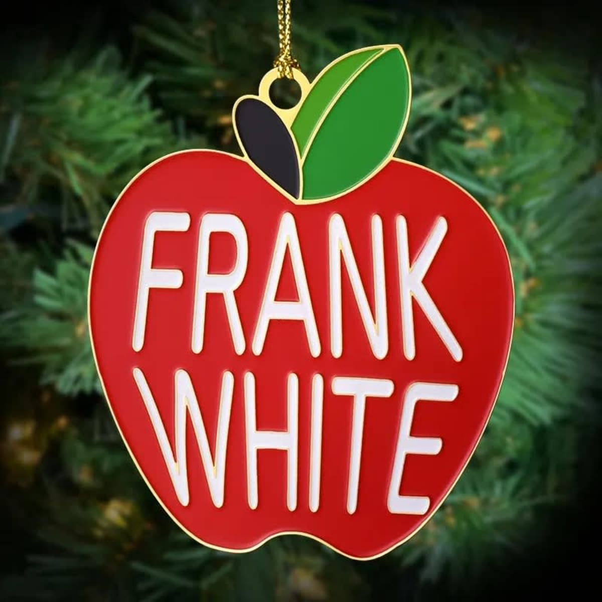 A red apple-shaped ornament with white text and a green leaf, featuring a logo on a gold chain.