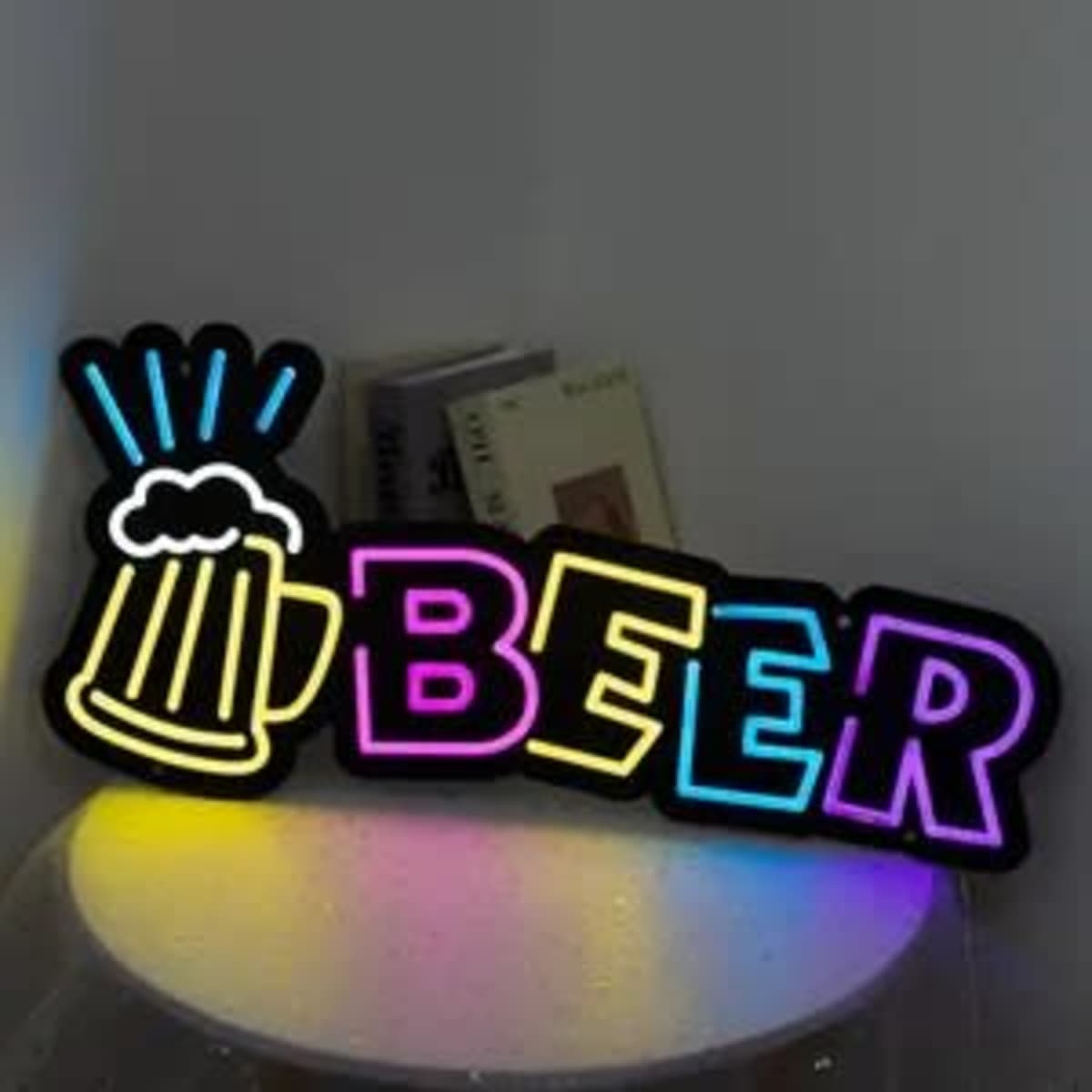 A neon sign featuring the word "BEER" in vibrant colours, with a beer mug illustration, set against a neutral background.