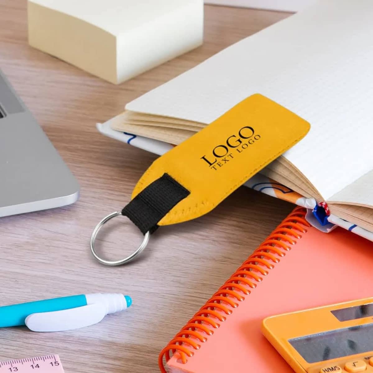 A yellow neoprene floating keychain rests on an open notebook, surrounded by stationery items.