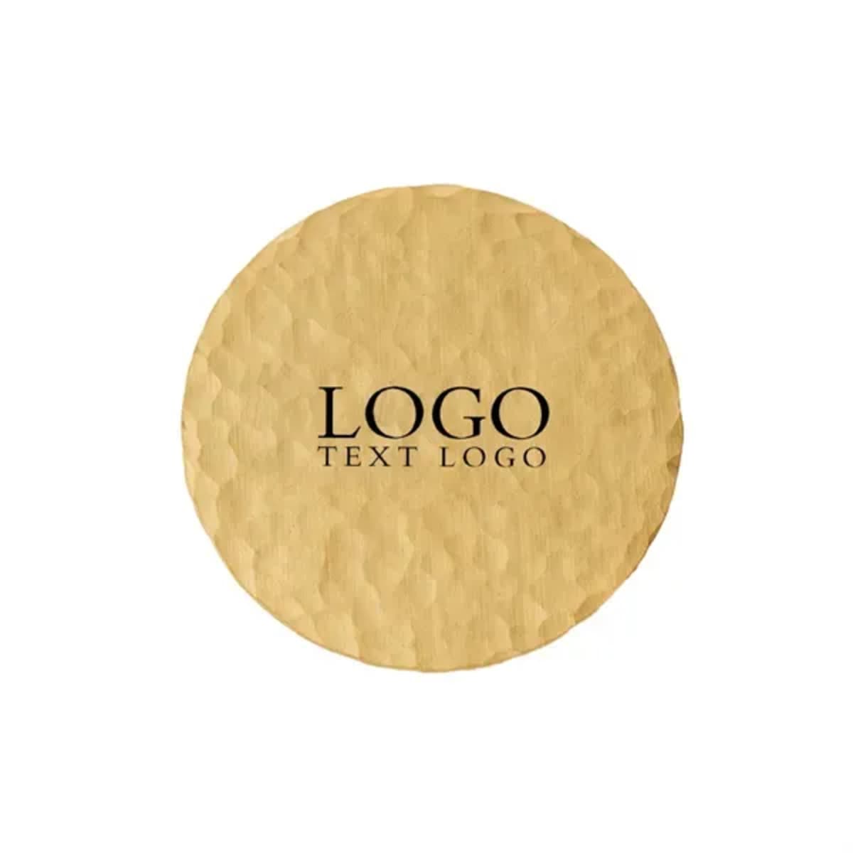 A round brass name badge with a textured surface and a logo. The badge features a gold tone.