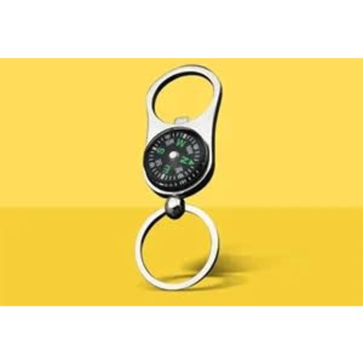 A silver portable bottle opener with a built-in compass, attached to a keychain, set against a yellow background.