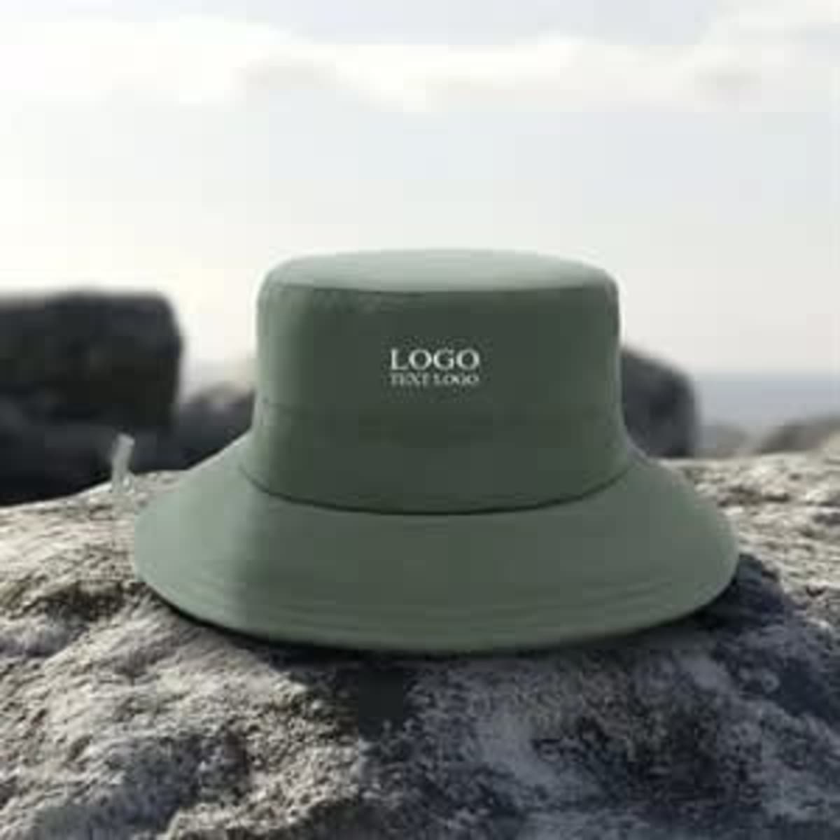 A green foldable bucket hat with a logo rests on a stone surface against a blurred outdoor background.