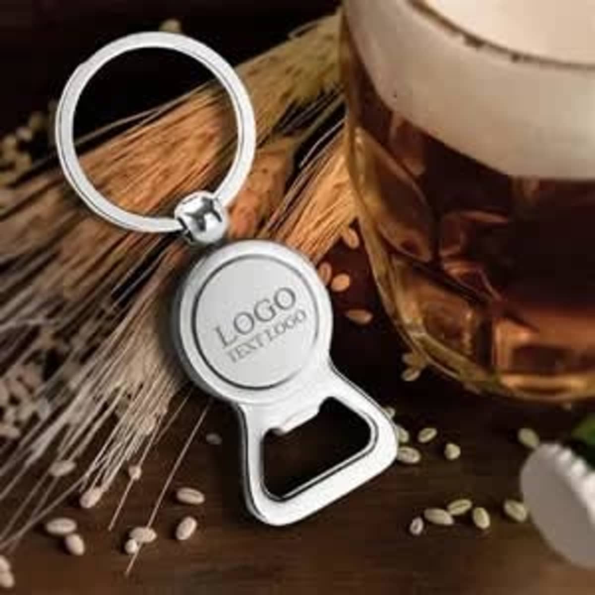A drink bottle opener keychain in chrome sits beside a glass of beer, with a logo visible on the keychain.