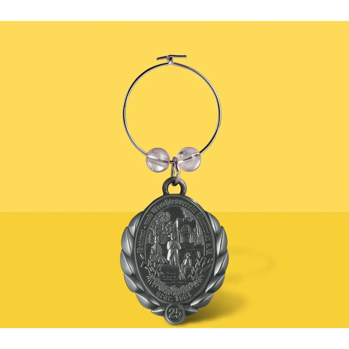 A 3D die cast wine charm in silver with a decorative medallion and circular hoop. Features two clear beads.