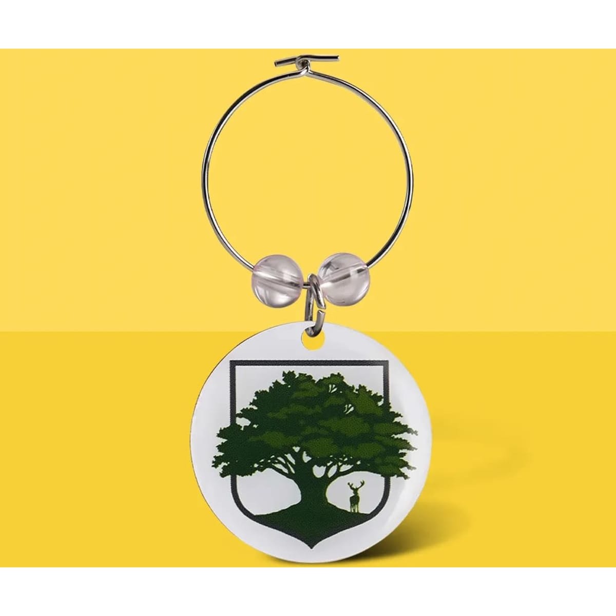 A wine charm featuring a circular white pendant with a green tree design and a silver hoop.