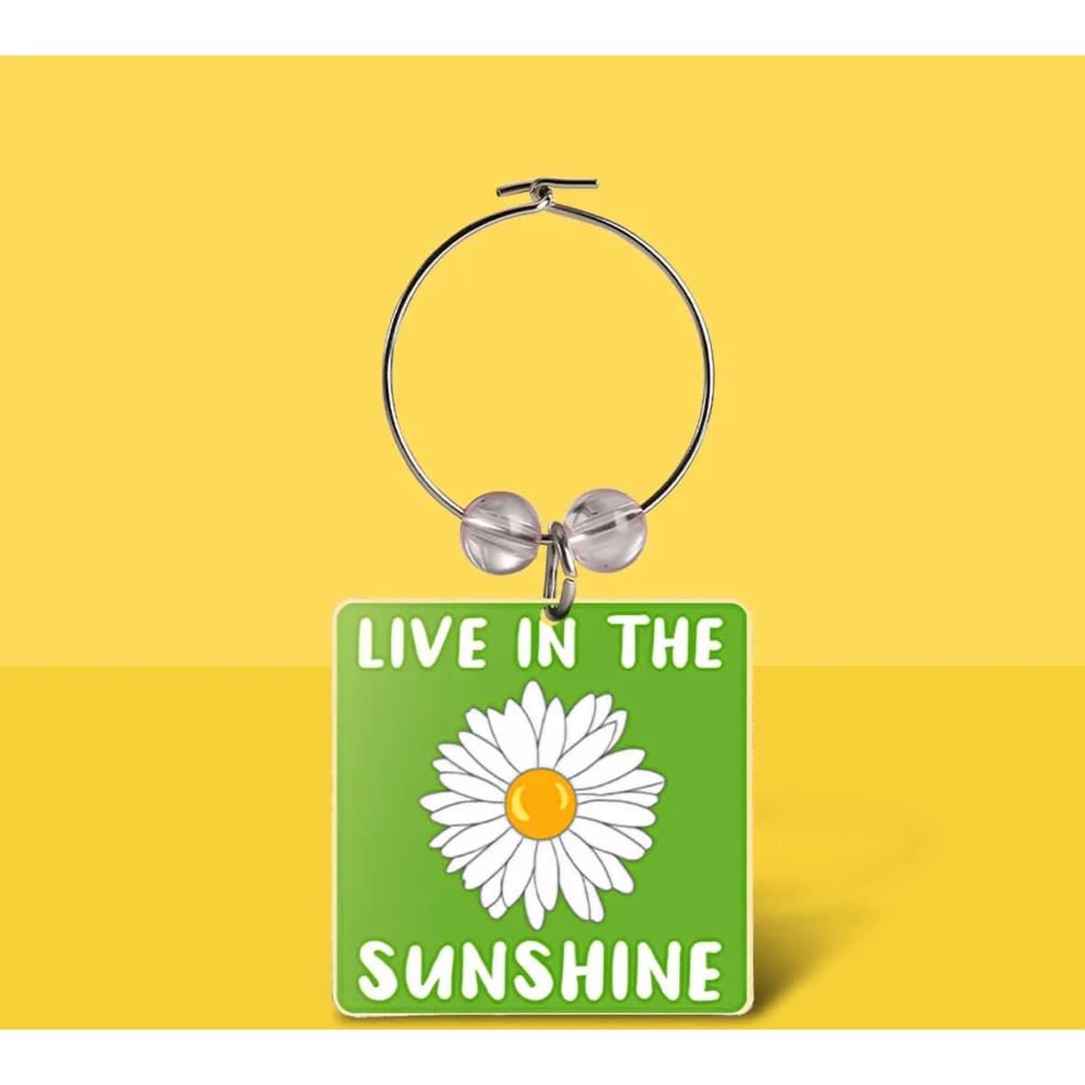 A drink bottle charm featuring a square green tag with a daisy design and a silver hoop.