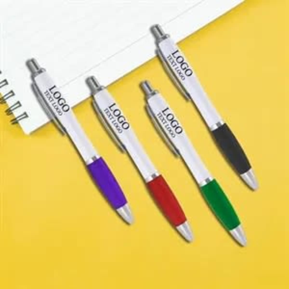 A set of four plastic pens in purple, red, green, and black, with a logo on each pen, next to a notepad.