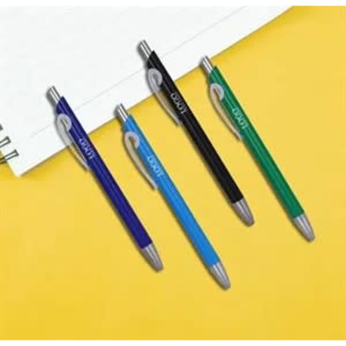 A set of four solid plastic ballpoint pens in blue, black, green, and purple, placed beside a notepad on a yellow background.