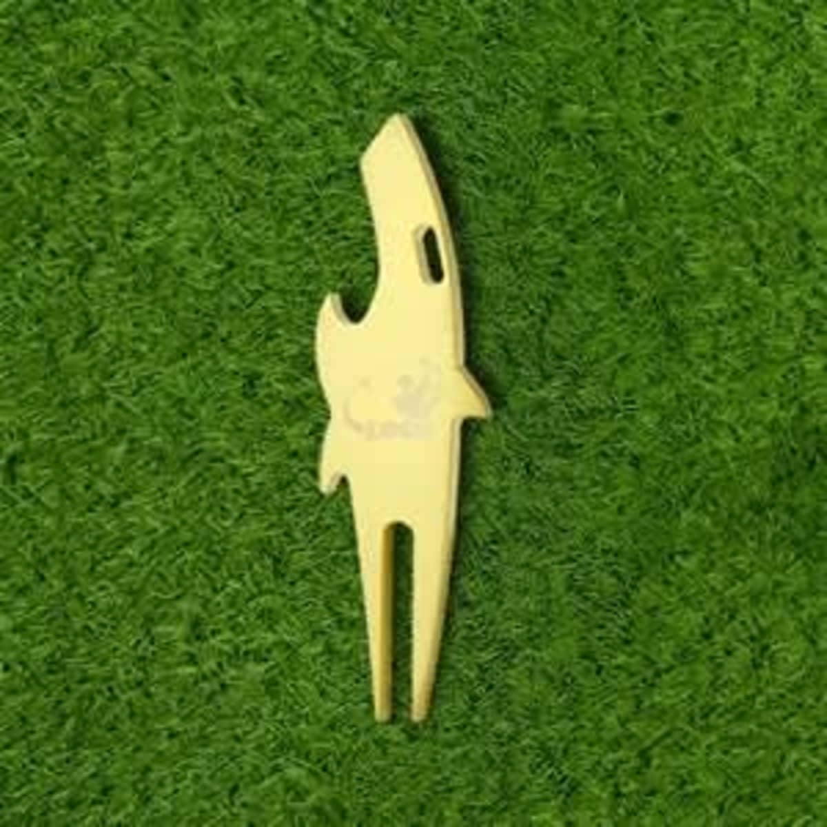A yellow divot tool shaped like a shark, positioned on green grass. The tool features a branding logo.