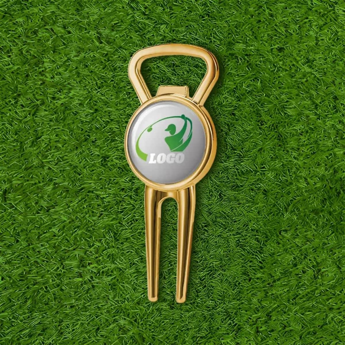 A gold metal divot tool and beer bottle opener with a circular logo, placed on green grass.