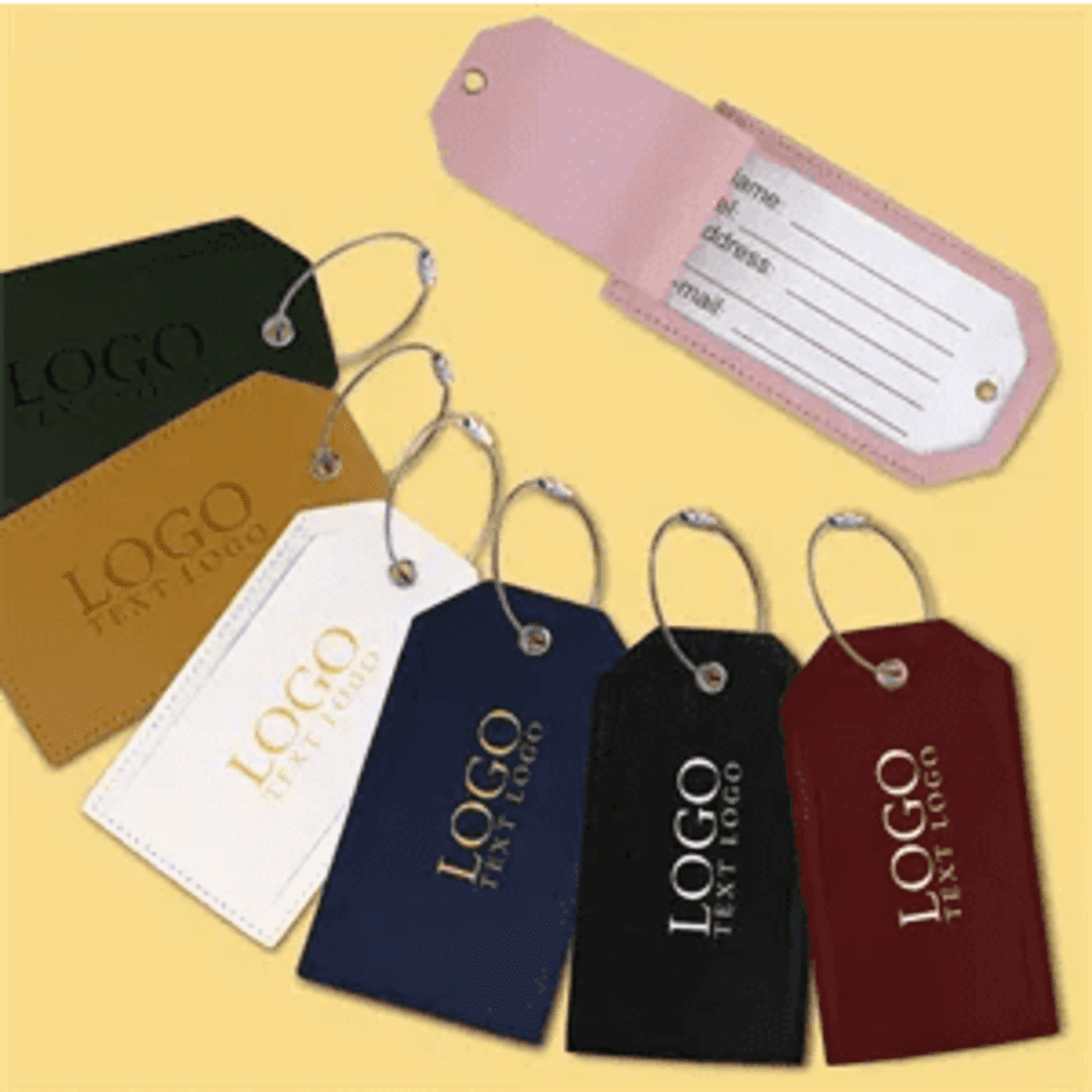 A set of soft vegan leather luggage tags in various colours, featuring a logo, with a pink tag showing a writable section.