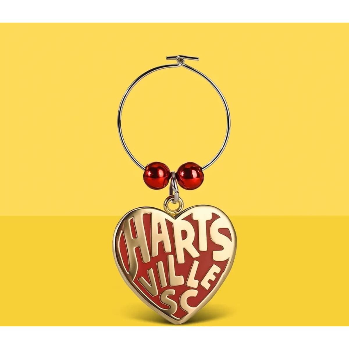 A drink charm featuring a red heart with white lettering and red beads, attached to a metal hoop with a logo.